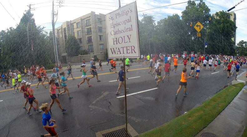 Some runners go for a quick blessing under the holy water sprinkler at the Cathedral of St. Philip as they make their way down Peachtree Road in Buckhead during the AJC Peachtree Road Race on July 4, 2014. AJC FILE PHOTO