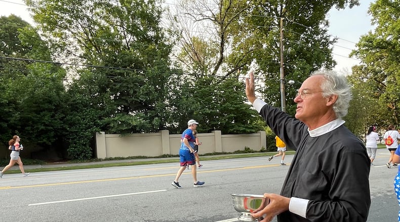The Rev. Sam Candler of the Cathedral of St. Philip blessed runners with holy water. (Photo: Anjali Huynh/AJC)