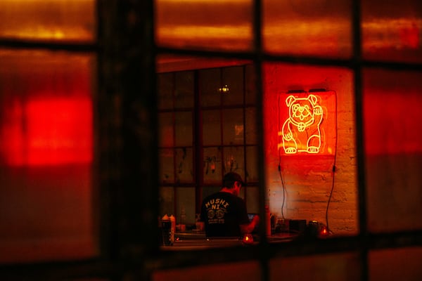A shot through an exterior window that shows a neon sign of a waving dog on mounted high on the wall with an employee wearing a Mushi Ni shirt facing away from the camera.