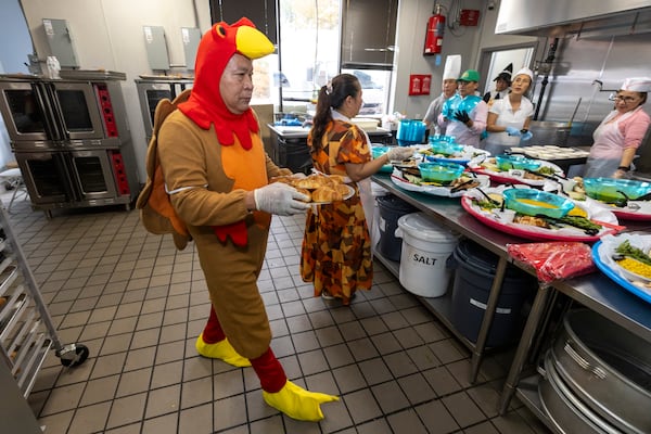 A server wearing a turkey costume helps put together platters of food during the Thanksgiving celebration. (Jason Getz/AJC)