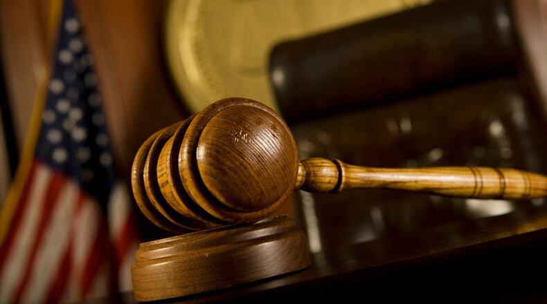 A judge's gavel up close, with the judge's chair, the American flag, and the courtroom seal in the background.