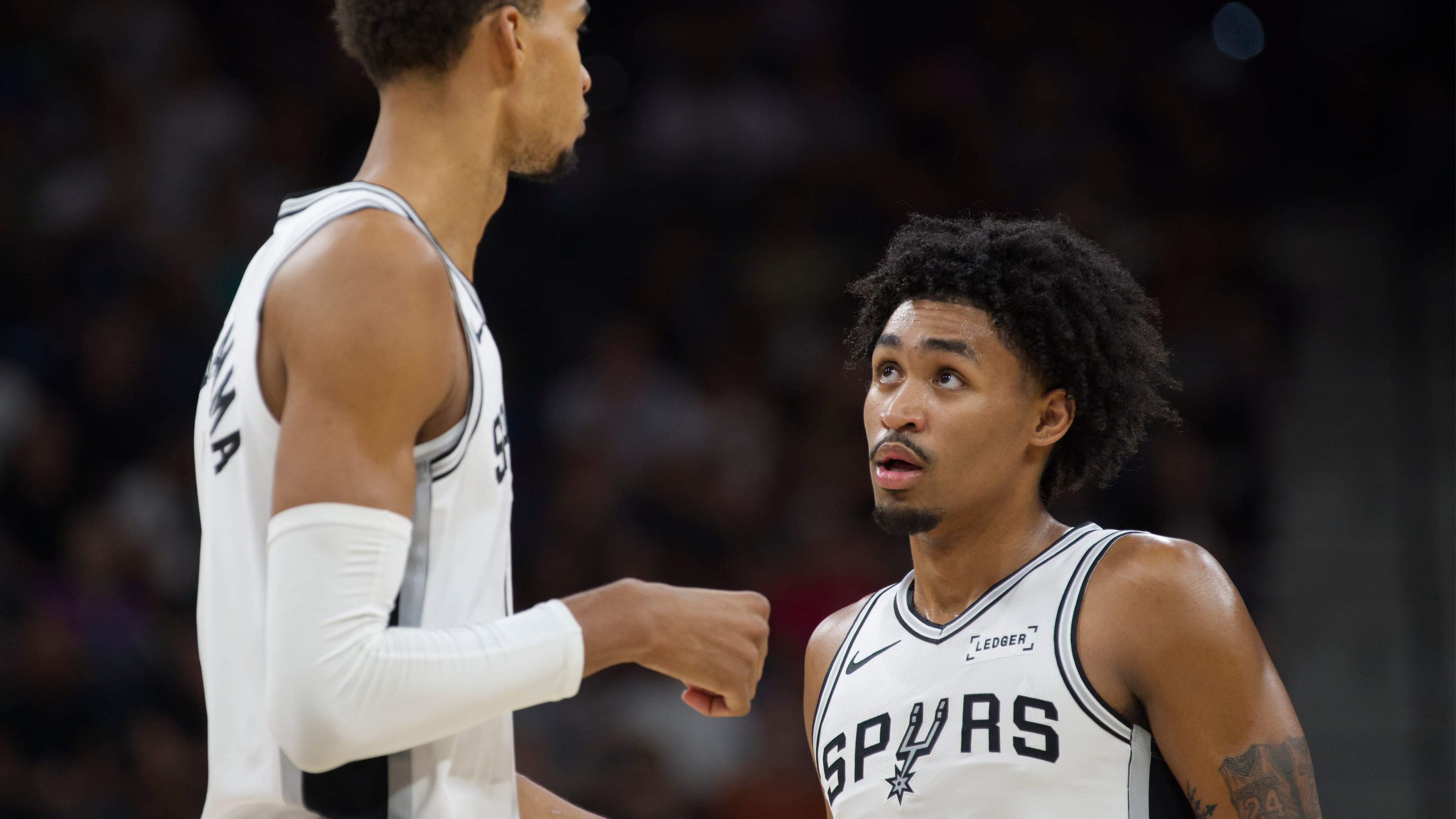 San Antonio Spurs center Victor Wembanyama, left, speaks with teammate Dylan Harper, right, during the first half of a preseason NBA basketball game against the Utah Jazz, Friday, Oct. 10, 2025, in San Antonio. (AP Photo/Darren Abate)
