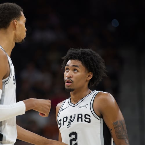 San Antonio Spurs center Victor Wembanyama, left, speaks with teammate Dylan Harper, right, during the first half of a preseason NBA basketball game against the Utah Jazz, Friday, Oct. 10, 2025, in San Antonio. (AP Photo/Darren Abate)