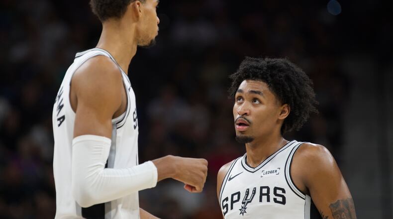 San Antonio Spurs center Victor Wembanyama, left, speaks with teammate Dylan Harper, right, during the first half of a preseason NBA basketball game against the Utah Jazz, Friday, Oct. 10, 2025, in San Antonio. (AP Photo/Darren Abate)