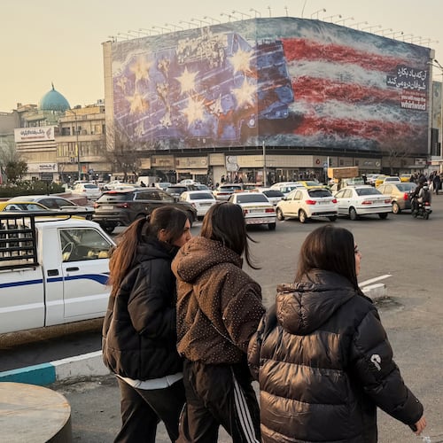 People walk in front a billboard with graphic showing a U.S aircraft carrier with damaged fighter jets on its deck, and sign reading in Farsi and English: "If you sow the wind, you'll reap whirlwind," at the Enqelab-e-Eslami (Islamic Revolution) square, in Tehran, Iran, Sunday, Jan. 25, 2026. (AP Photo/Vahid Salemi)