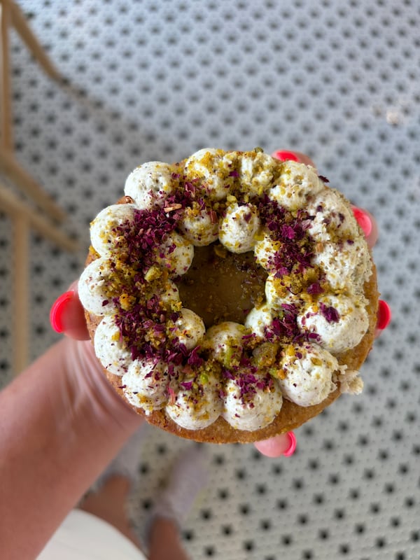 A hand holds a highly decorated, personal-sized tart from below, with the photo taken from above.