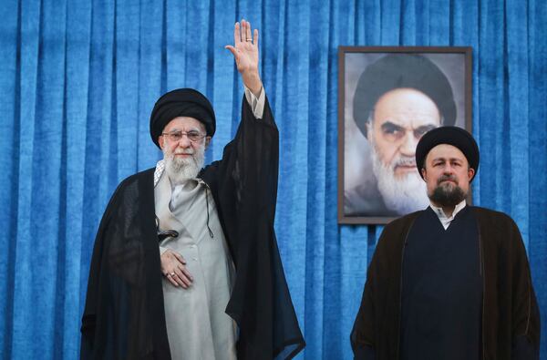 In this photo released by the official website of the office of the Iranian supreme leader, Supreme Leader Ayatollah Ali Khamenei waves to the crowd as he arrives for a ceremony marking the anniversary of the 1989 death of the late revolutionary founder Ayatollah Khomeini, shown in the poster in background, as Ayatollah Khomeini's grandson Hassan stands at right, at his shrine just outside Tehran, Iran, Wednesday, June 4, 2025. (Office of the Iranian Supreme Leader via AP)
