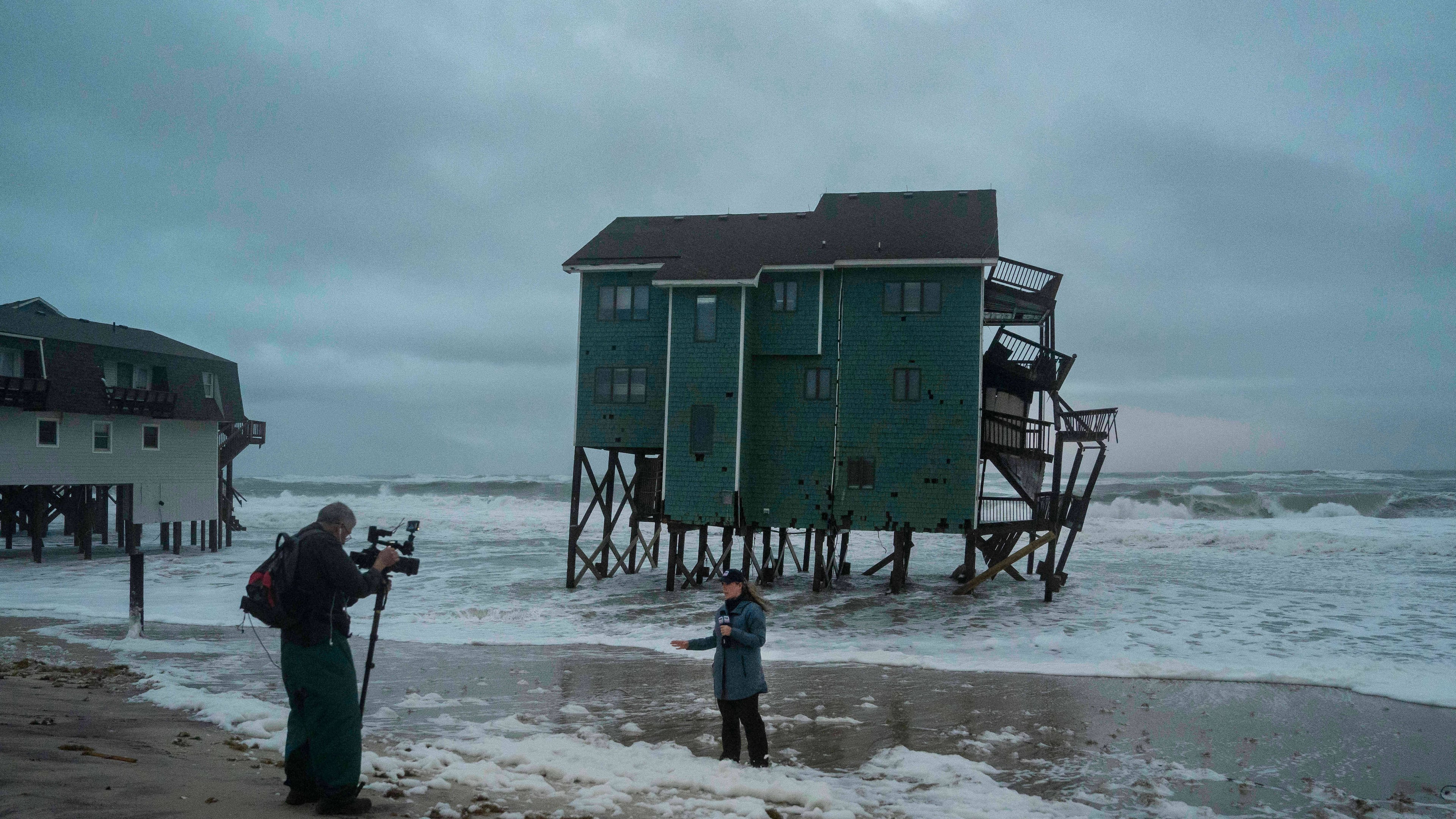 A Fox Weather reporter films in front of a house at risk of collapse in the midst of a storm, Sunday, Oct. 12, 2025, in Buxton, N.C. (AP Photo/Allison Joyce)