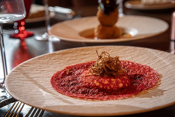 A sidelong look at a large plate holding a piece of burrata cheese covered with and surrounded by a red sauce.