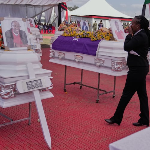 A mourner reacts as she stands between caskets carrying the remains of the 16 girls who died in the Utumishi Academy school fire during a memorial service at Gilgil Stadium, Nakuru County, Kenya, Friday, June 12, 2026. (AP Photo/Brian Inganga)