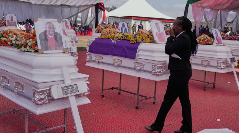 A mourner reacts as she stands between caskets carrying the remains of the 16 girls who died in the Utumishi Academy school fire during a memorial service at Gilgil Stadium, Nakuru County, Kenya, Friday, June 12, 2026. (AP Photo/Brian Inganga)