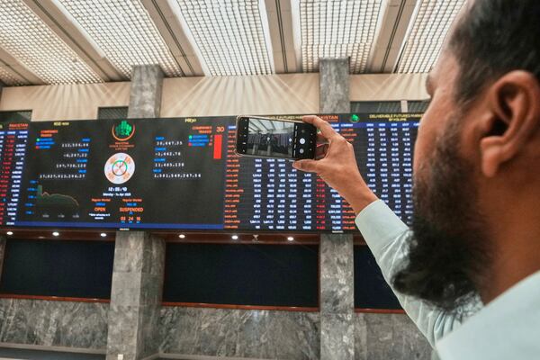 An investor takes a picture with a cell phone of indexes and benchmark 100 index at the Pakistan Stock Exchange (PSE), in Karachi, Pakistan, Monday, April 7, 2025. (AP Photo/Fareed Khan)
