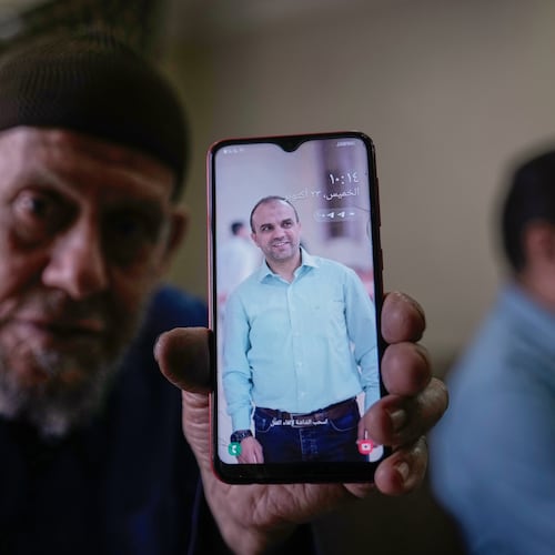 Waleed Husein Ali, shows a picture on a phone of his son, Mohammad, 45, who died in Israeli custody at the Kishon detention center, as he sits in the family's living room in the Nur Shams refugee camp near the West Bank town of Tulkarem, Thursday, Oct. 23, 2025. (AP Photo/Majdi Mohammed)