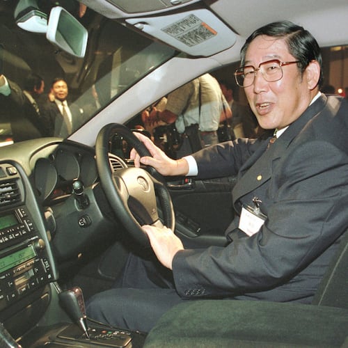 FILE - Hiroshi Okuda, then, president of Toyota Motor Corp., smiles as he sits at the steering wheel of the "Aristo," Toyota's remodeled sports sedan during a press conference at a Tokyo hotel, Aug. 27, 1997. (AP Photo/Shizuo Kambayashi, File)