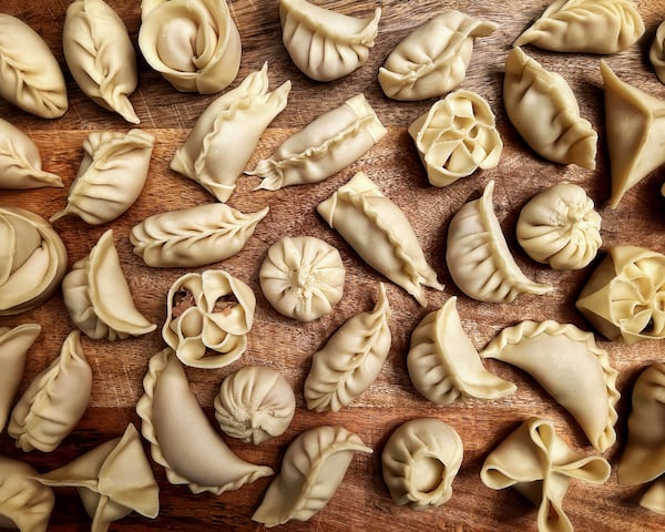 various dumplings displaying different folding techniques on a wooden cutting board.