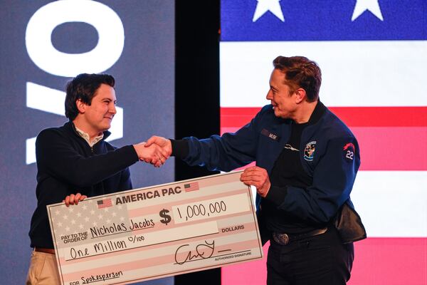Elon Musk presents a check for $1 million dollars to a man during a town hall Sunday, March 30, 2025, in Green Bay, Wis. (AP Photo/Jeffrey Phelps)