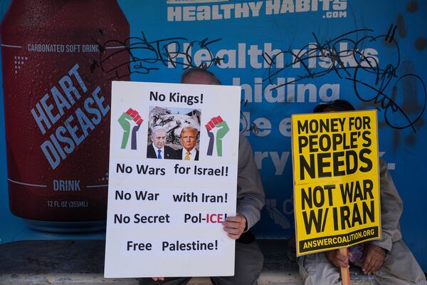 Two anti-war demonstrators hold signs at a bus stop outside the Wilshire Federal Building in Los Angeles Sunday, June 22, 2025, following U.S. airstrikes on Iran's nuclear facilities. (AP Photo/Jae C. Hong)