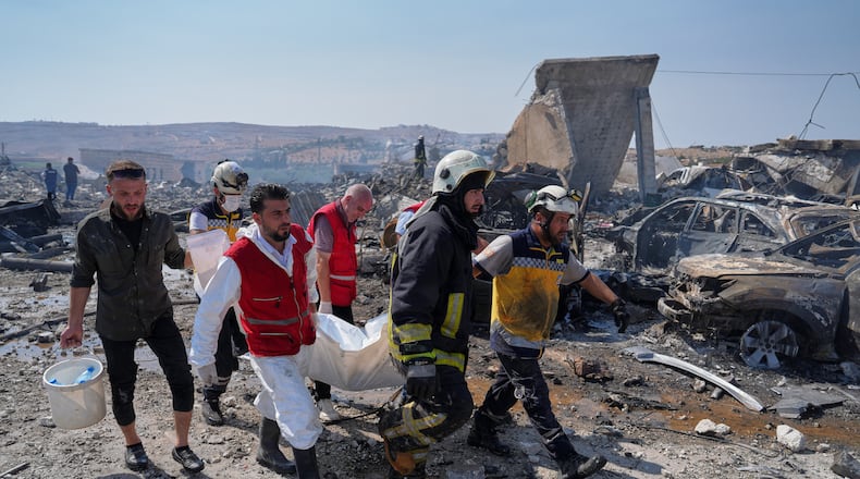 Civil defense workers and a firefighter remove a body from the site of an explosion at what Syria's Defense Ministry said was a warehouse used for the temporary storage of weapons near Sarmada, in Idlib province, Syria, Wednesday, Sept. 9, 2026. (AP Photo/Omar Albam)