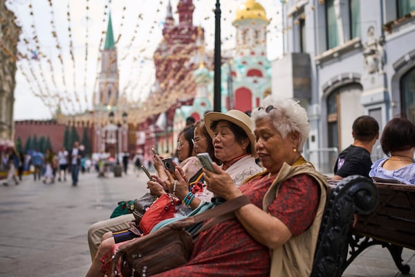 Tourists sitting near the Kremlin in Moscow look at their phones on Wednesday, July 16, 2025. (AP Photo/Alexander Zemlianichenko)