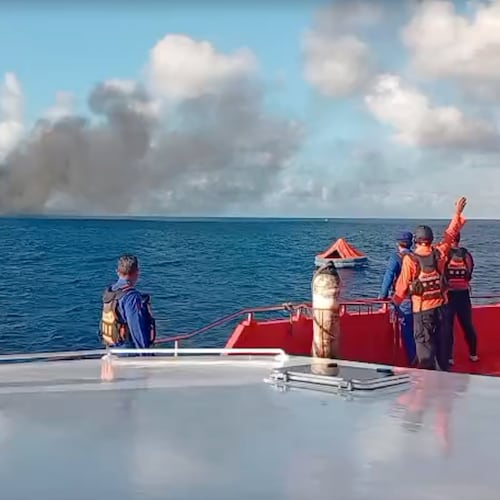 In this image made from video released by the Indonesian National Search and Rescue Agency (BASARNAS), the crew of a rescue ship look on as smoke billows from a passenger ferry that caught fire while traveling from the tourist island of Bali to neighboring island of Lombok, in the waters of Lombok Strait, Indonesia, Wednesday, Aug. 12, 2026. (BASARNAS via AP)