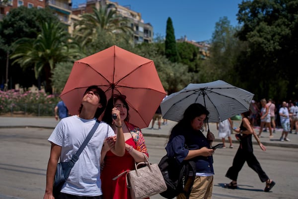 Tourists protect themselves from the sun with umbrellas while looking at the Sagrada Familia church on a hot day in Barcelona, Spain, Monday, June 30, 2025. (AP Photo/Emilio Morenatti)