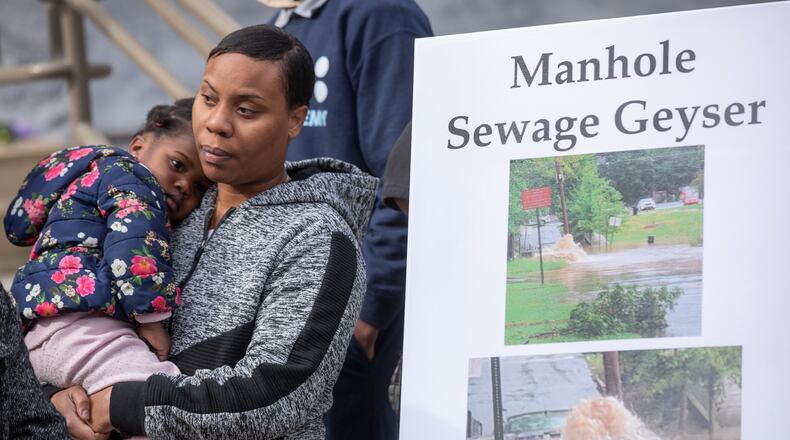 Westside families stand next to photos of sewage spills and flooded homes during a press conference to announce a lawsuit against the city of Atlanta over flooding issues on Feb. 29, 2024.