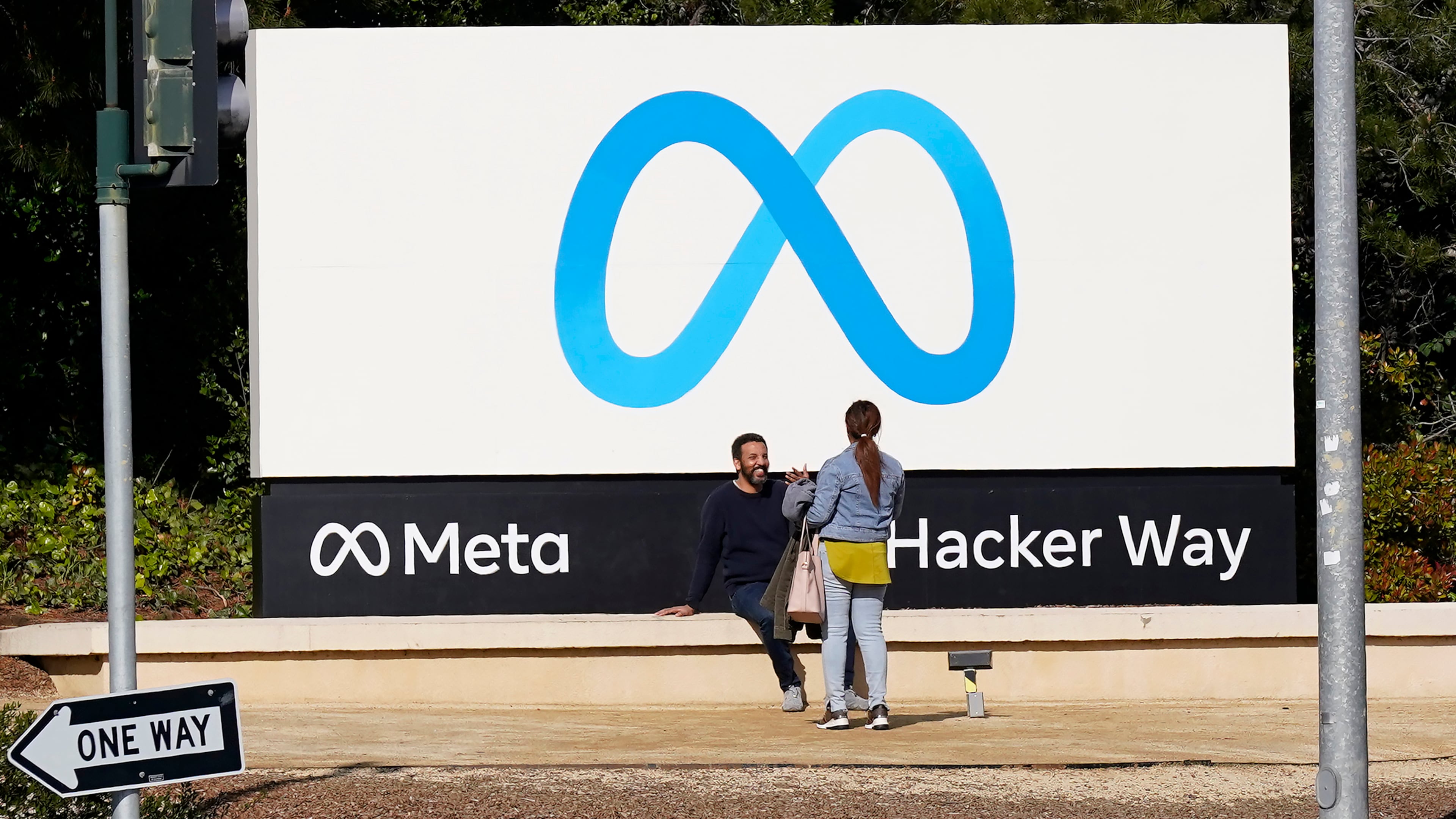 FILE - People talk near a Meta sign outside of the company's headquarters in Menlo Park, Calif., March 7, 2023. (AP Photo/Jeff Chiu, File)