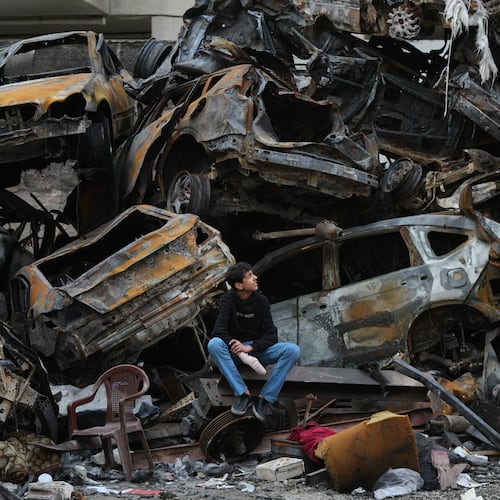 A man sits next to charred cars and wreckage where a building was destroyed by an Israeli airstrike the previous Wednesday, in central Beirut, Lebanon, Tuesday, April 14, 2026. (AP Photo/Hassan Ammar)