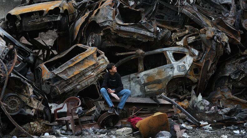 A man sits next to charred cars and wreckage where a building was destroyed by an Israeli airstrike the previous Wednesday, in central Beirut, Lebanon, Tuesday, April 14, 2026. (AP Photo/Hassan Ammar)