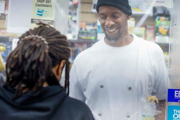 Overnight store clerk Connell Daniels Jr. interacts with a customer from behind bulletproof glass at JJ Food Mart on Atlanta's west side Thursday. (Miguel Martinez/AJC)