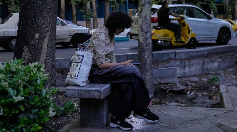 A woman checks her smartphone while sitting on a bench along a sidewalk in northern Tehran, Iran, Tuesday, May 26, 2026. (AP Photo/Vahid Salemi)