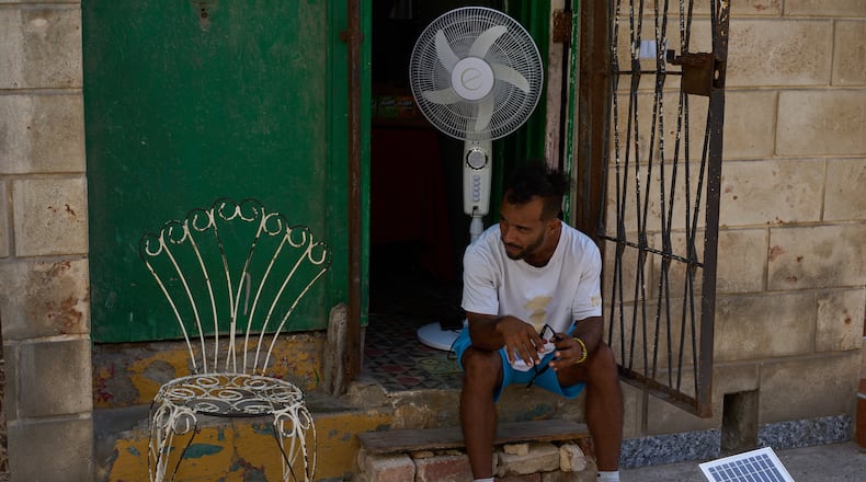 A man charges his fan's battery at his doorway using a small solar panel set up on the street during a blackout in Havana, Cuba, Friday, Sept. 18, 2026. (AP Photo/Ramon Espinosa)