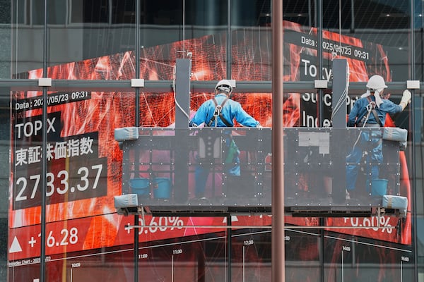 Workers clean the glass window of a building in front of an electronic stock board showing Japan's TOPIX index at a securities firm Friday, May 23, 2025, in Tokyo. (AP Photo/Eugene Hoshiko)
