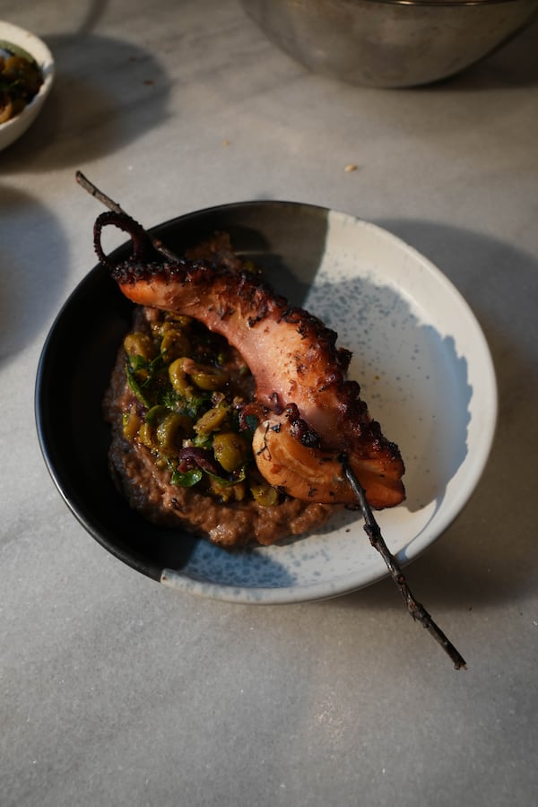 A dish of grilled octopus, with an a charred octopus tentacle skewered by a blackened wooden skewer