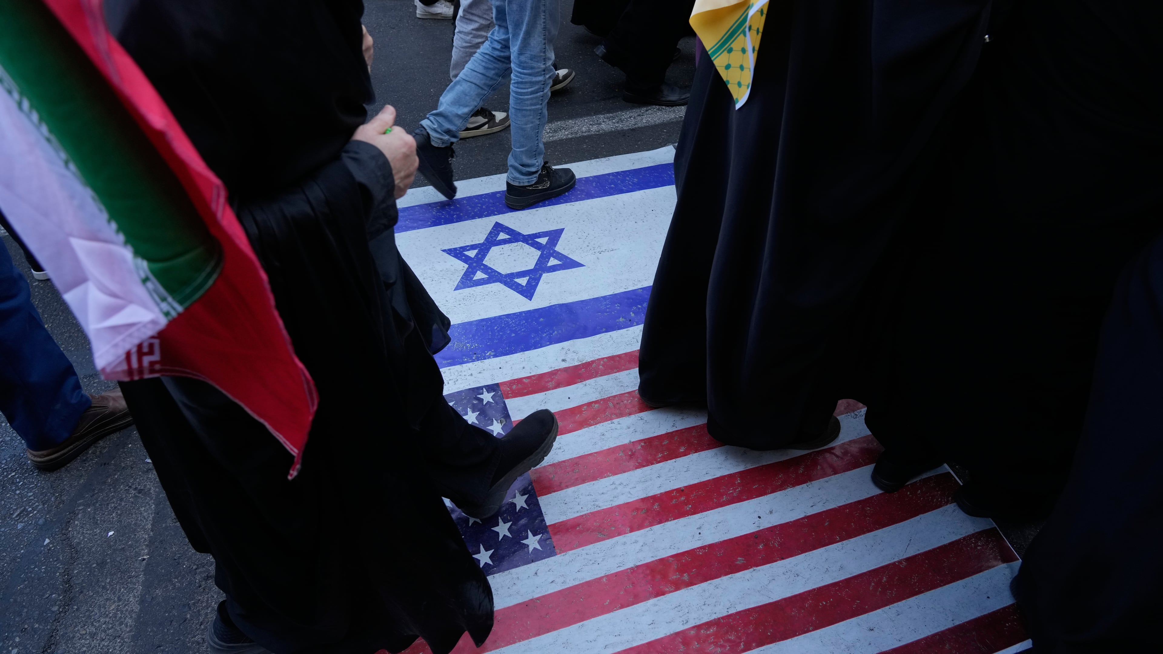 Demonstrators walk on a representation of the U.S. and Israeli flags during an annual rally in front of the former U.S. Embassy in Tehran, celebrating the anniversary of the 1979 takeover of the embassy, Iran, Tuesday, Nov. 4, 2025. (AP Photo/Vahid Salemi)