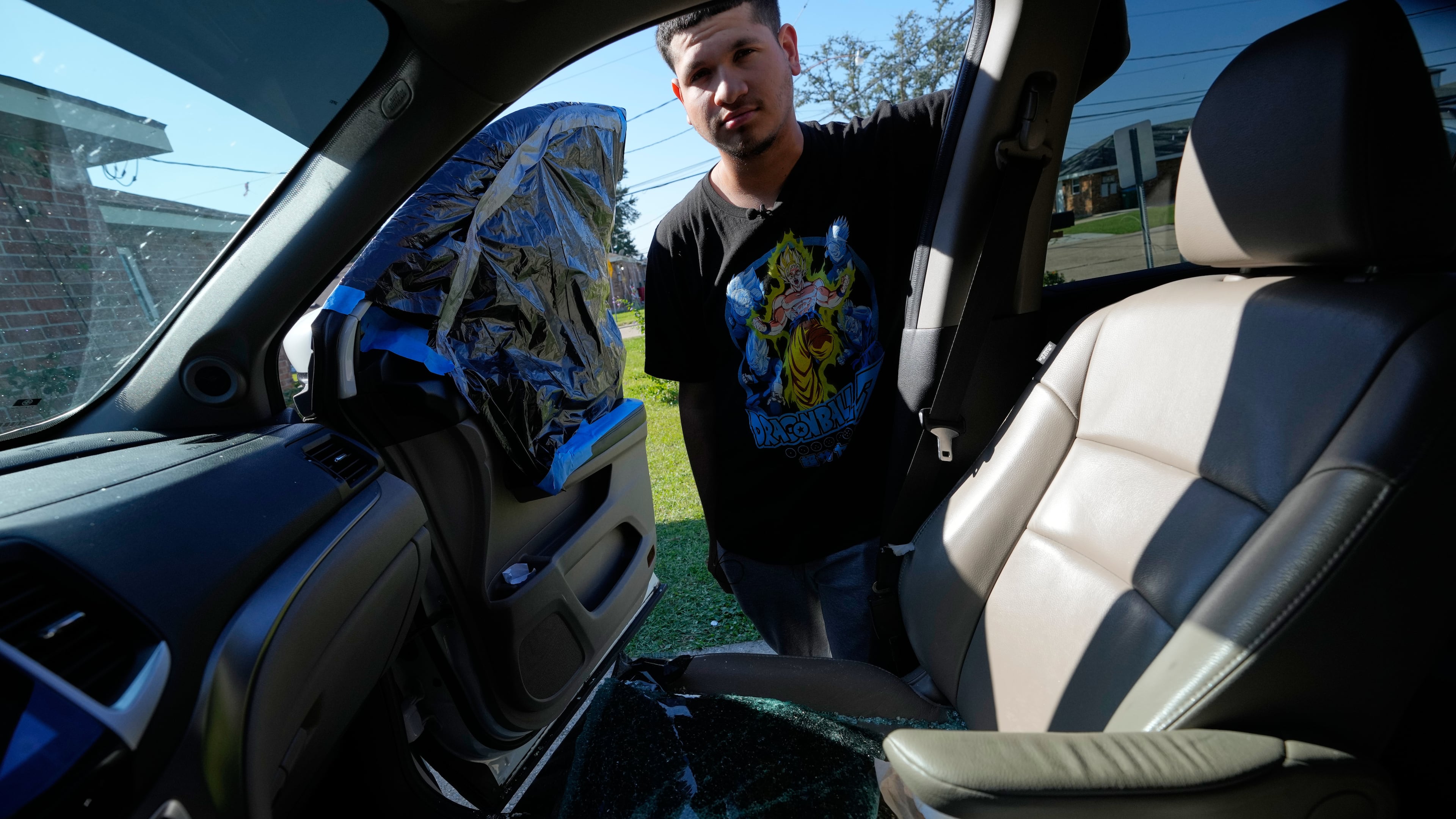 Jonathan Escalante stands over the broken window of his mother's car, which was shattered by federal immigration agents who took her away, during a federal immigration crackdown in Kenner, La., Tuesday, Dec. 9, 2025. (AP Photo/Gerald Herbert)