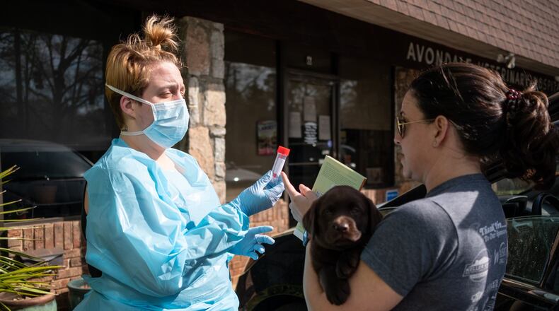 Rita Harrell picks up her 8-week-old puppy Tally from Abby Mosconi in the parking lot of Avondale Veterinary Hospital. Harrell said her family got Tally to help make the coming weeks of social distancing easier. Meanwhile, Avondale Veterinary Hospital was taking extra precautions, such as having their staff meet clients in the parking lot rather than clients coming into the office. BEN@BENGRAY.COM FOR THE ATLANTA JOURNAL-CONSTITUTION
