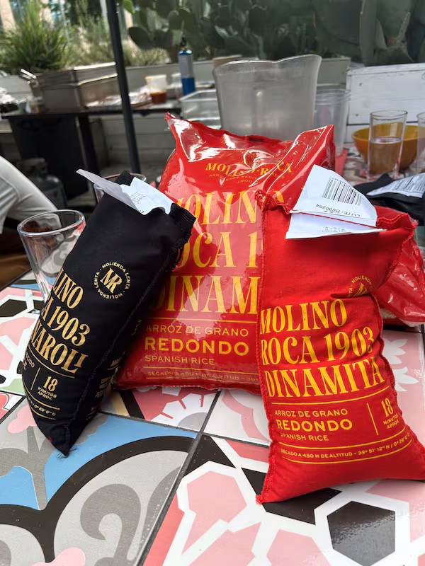 One black sack of rice, and two red sacks of rice, all on top of a colorful tiled table.