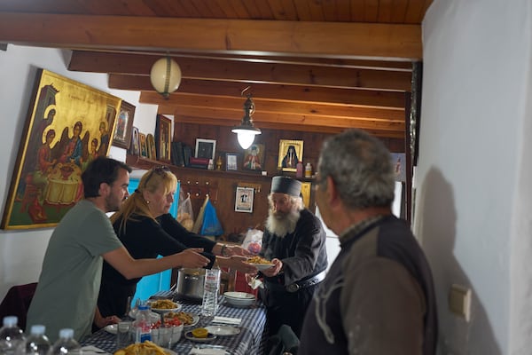 From left, Constantin Papakonstantinou, an assistant residing at the monastery, Ioanna Kape, Head of the Amorgos Port Authority, and Christian Orthodox monk Father Spyridon of Amorgos, as dinner is served at the Monastery of Panagia Hozoviotissa on Thursday, March 27, 2025. (AP Photo/Petros Giannakouris)