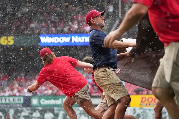 Members of the Busch Stadium grounds crew unfurl a tarp over the field at the start of a rain delay during the third inning of a baseball game between the St. Louis Cardinals and the Atlanta Braves Sunday, July 13, 2025, in St. Louis. (AP Photo/Jeff Roberson)