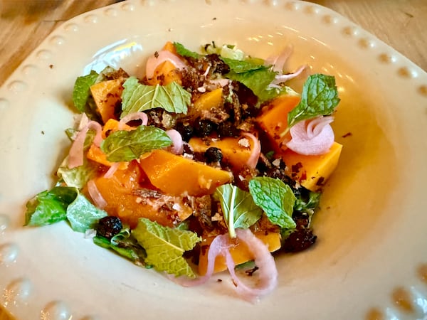 A colorful squash salad garnished with fresh basil on a shallow restaurant bowl.