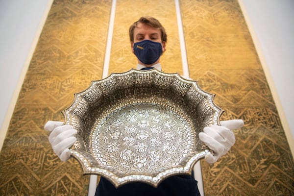FILE - An employee at Sotheby's auction house holds a twelfth-century silver inlaid scalloped basin with astrological designs, estimated to fetch 1,000,000 - 1,500,000 sterling pounds, as part of the auction house's forthcoming Arts of the Islamic World and India sale on March 31, in London, March 29, 2021. (Dominic Lipinski/PA via AP)