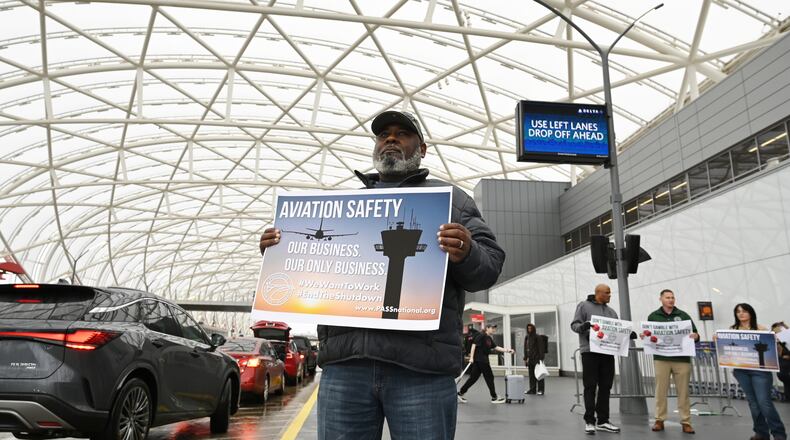 John Love — a member of the Professional Aviation Safety Specialists, AFL-CIO union — holds a sign with other PASS members at Hartsfield-Jackson Atlanta International Airport's domestic terminal on Wednesday, Oct. 29, 2025. PASS members at the Federal Aviation Administration working without pay or furloughed share pamphlets to call public attention to the impact of the government shutdown on aviation safety and the personal toll it is taking on their families. (Hyosub Shin/AJC)