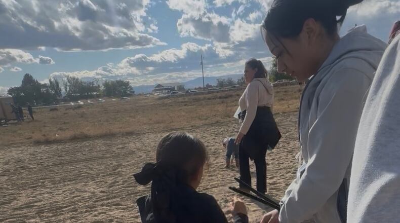 This photo provided by Anabel Romero shows her 14-year-old daughter, right, with her hands zip-tied, next to her 8-year-old daughter, foreground center, during a raid by various law enforcement agencies at La Catedral Arena horse race track in Wilder, Idaho, on Oct. 19, 2025. (Anabel Romero via AP)