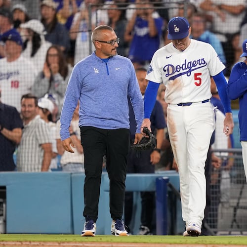 Los Angeles Dodgers first baseman Freddie Freeman, center, walks back on to the field accompanied by manager Dave Roberts, right, and trainer Greg Barajas after he fell into the dugout while trying to catch a foul ball hit by Kansas City Royals' Isaac Collins during the eighth inning of a baseball game Wednesday, Aug. 12, 2026, in Los Angeles. (AP Photo/Mark J. Terrill)