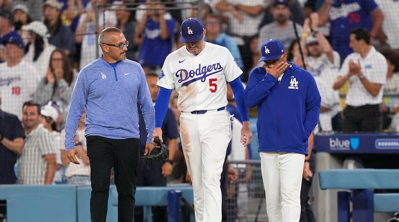 Los Angeles Dodgers first baseman Freddie Freeman, center, walks back on to the field accompanied by manager Dave Roberts, right, and trainer Greg Barajas after he fell into the dugout while trying to catch a foul ball hit by Kansas City Royals' Isaac Collins during the eighth inning of a baseball game Wednesday, Aug. 12, 2026, in Los Angeles. (AP Photo/Mark J. Terrill)