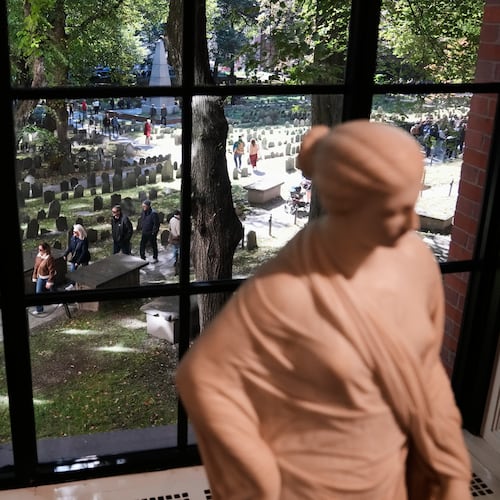 Visitors walk though the Granary Burying Ground, which includes the graves of John Hancock, Samuel Adams and Paul Revere, seen through a window at the Boston Athenaeum, Thursday, Oct. 9, 2025, in Boston. (AP Photo/Charles Krupa)