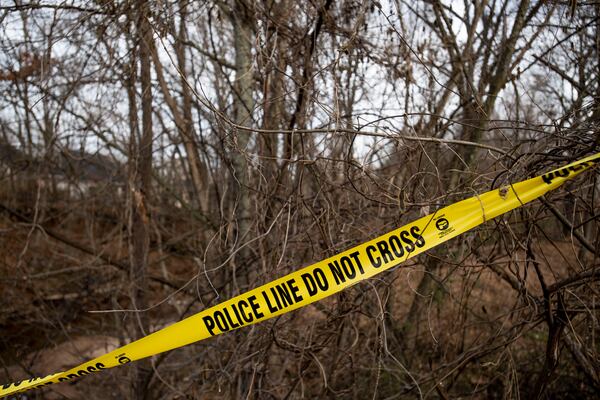 Stock image of police tape stretched across trees in a wooded area.