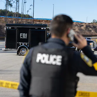 A police officer kept guard in front of crime scene tape as the FBI conducted a raid on the Fulton County Election Hub and Operation Center in Union City last week. (Arvin Temkar/AJC)