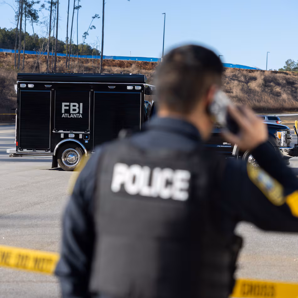 A police officer keeps guard in front of crime scene tape as the FBI conducts a raid on the Fulton County Election Hub and Operation Center in Union City on Wednesday, Jan. 28, 2026. (Arvin Temkar/AJC)